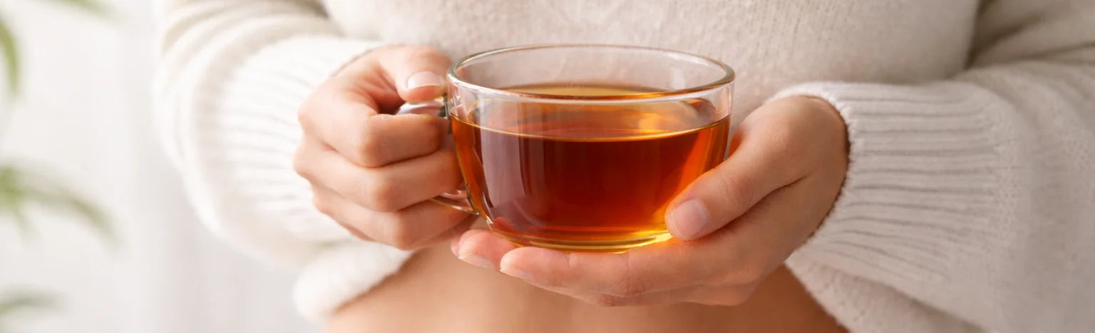 Glass cup of herbal tea with natural botanicals, arranged on a warm wooden surface, creating a clean and soothing wellness moment.
